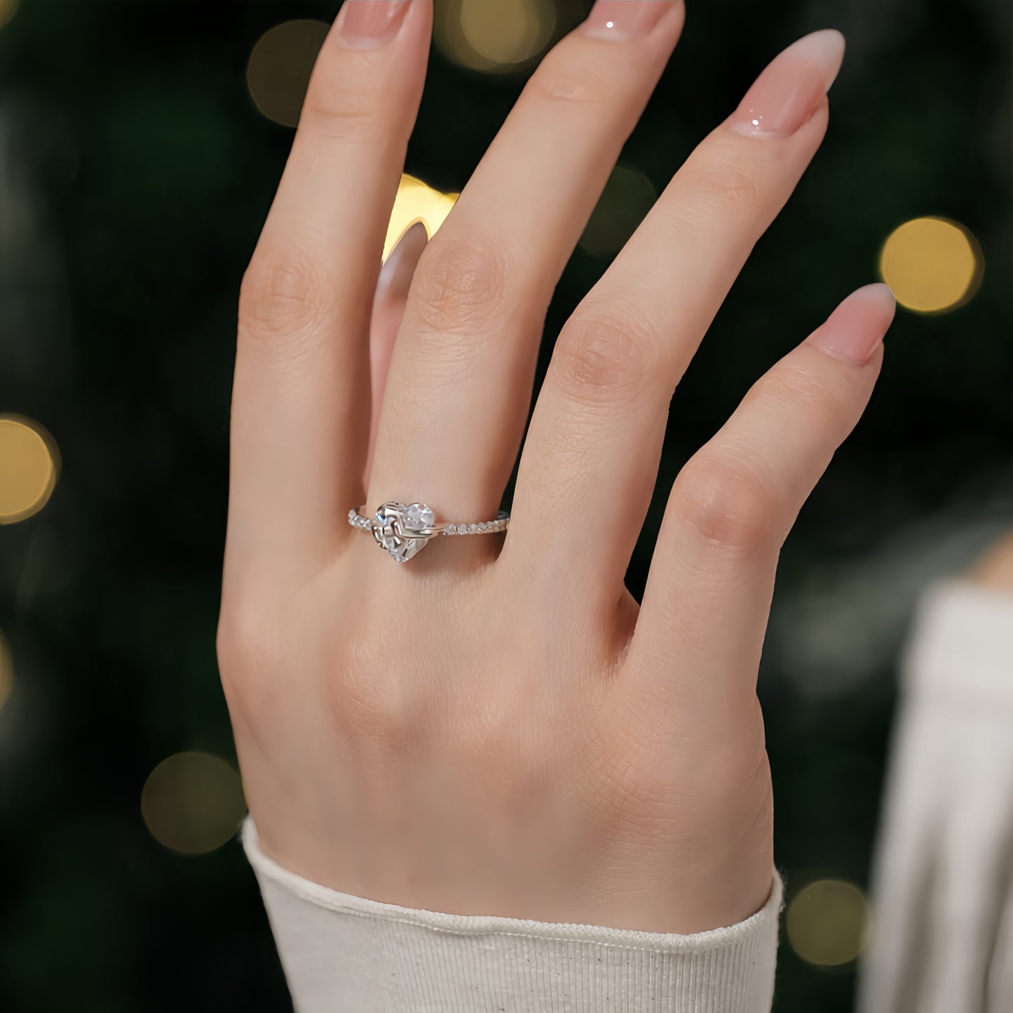 Hand wearing a diamond ring with a blurred festive background